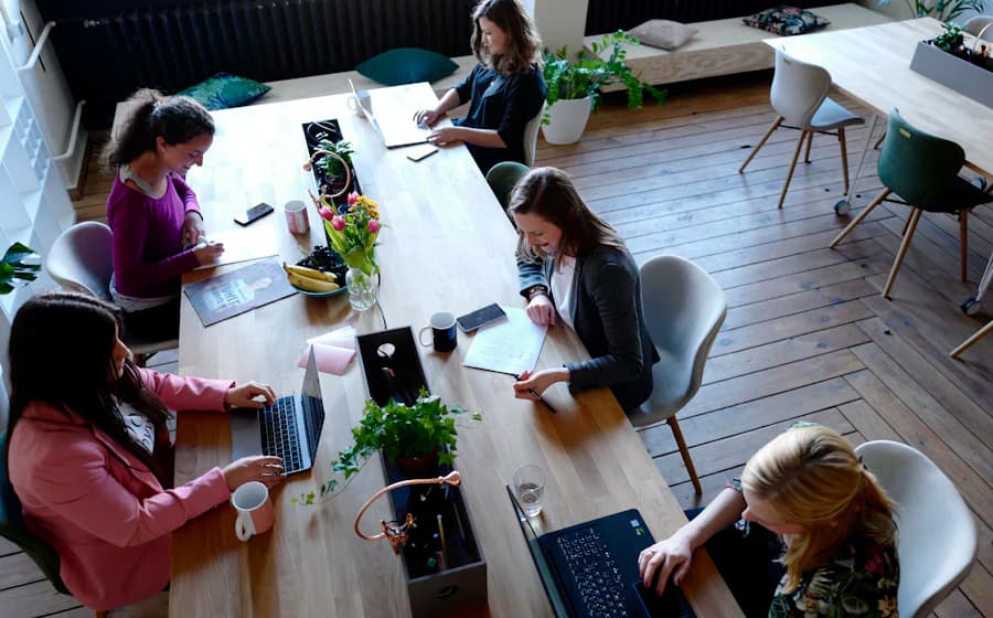 Overhead view of five people working on laptops at a long shared table in a bright office