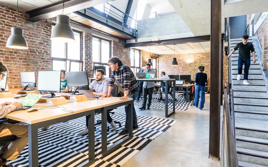 An open-plan brick-walled office with people working at desks near a metal staircase