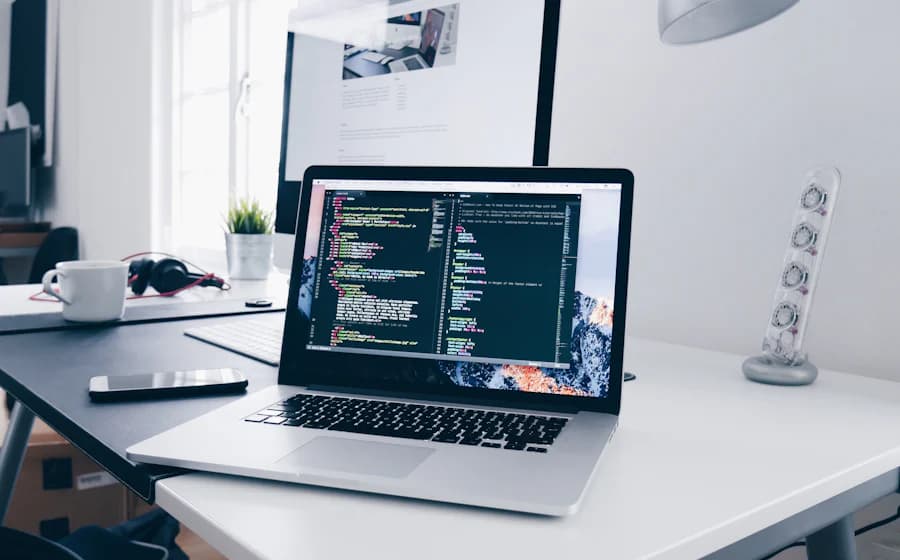 A laptop showing source code in an editor, on a desk beside a monitor and a coffee cup